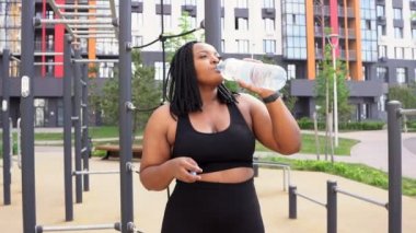 Kilolu bir kadın, şehirde koştuktan sonra su içiyor.