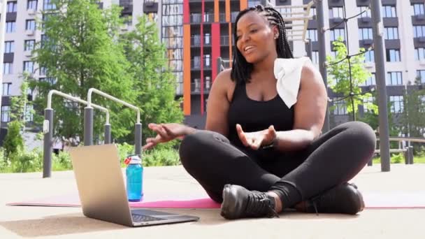 Junge Afroamerikanerin trainiert im Freien, während sie auf einer Yogamatte sitzt — Stockvideo