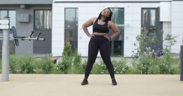プラスサイズアフリカ系アメリカ人女性ストレッチ足を演習を行う。都市の屋外で — ストック動画