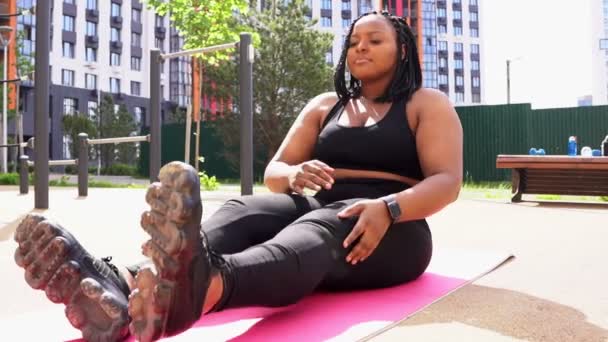 Jong plus size zwart afrikaanse vrouw stretching lichaam op mat alleen buiten, zijaanzicht — Stockvideo