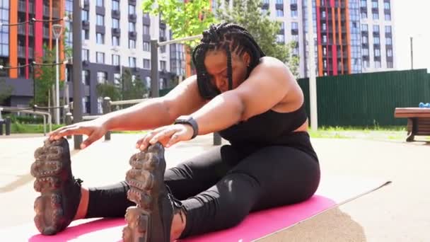 Fiatal plusz méret fekete afrikai nő nyújtás test szőnyeg szabadban csak, oldalnézet — Stock videók