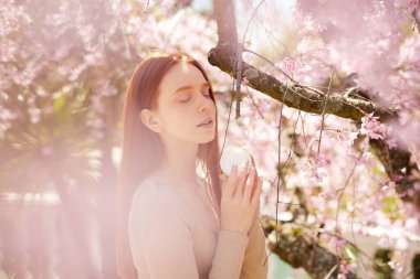 İlkbaharda çiçek açan ağaçta krema şişesiyle poz veren inanılmaz genç bir kadın.