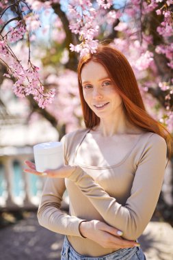 Tatmin olmuş bir kadın bahar, açık havada, bahçede yüz kremi kullanıyor.