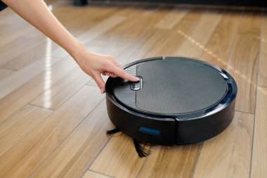 Siyah robot süpürge kullanan tanınmayan bir kadın, akıllı cihazdan memnun.