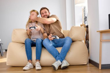 Çift evde video oyunu oynarken eğleniyor, ellerinde joysticklerle.