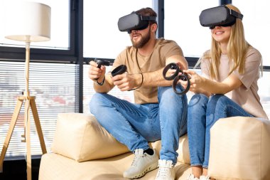 Sanal gerçeklik simülatörü kullanan güzel bir çift oturma odasında, yan görünümde oyunlar oynuyor.