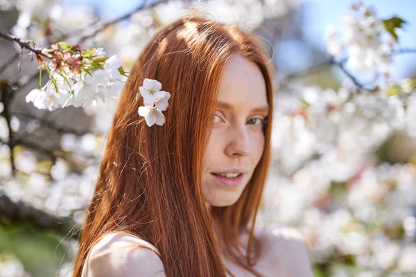 Rödhårig vacker kvinna njuter av blommande träd. Mode modell i Spring Garden. — Stockfoto