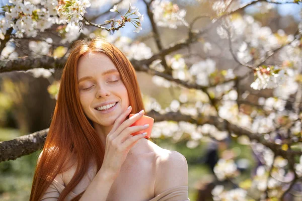 Charmante femme avec peau fraîche de santé tenant bouteille de crème dans les mains, dans la nature — Photo