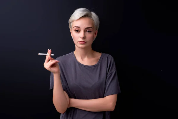 Mulher confiante segurando cigarro nas mãos, calmo e relaxado, usando tabaco, isolado em preto — Fotografia de Stock