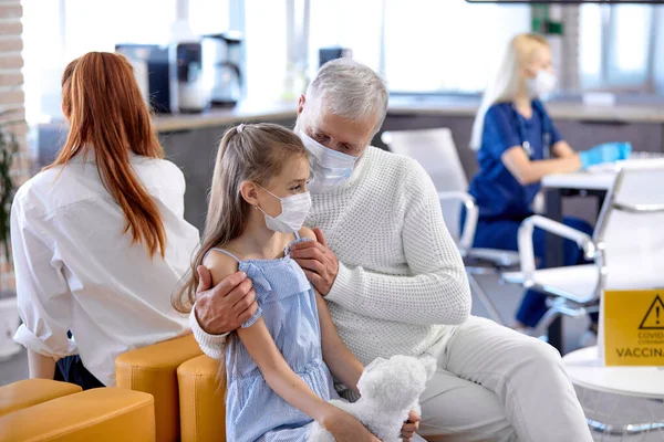 Äldre man har samtal med skrämd liten flicka i läkare kontor sutin mass vaccination — Stockfoto