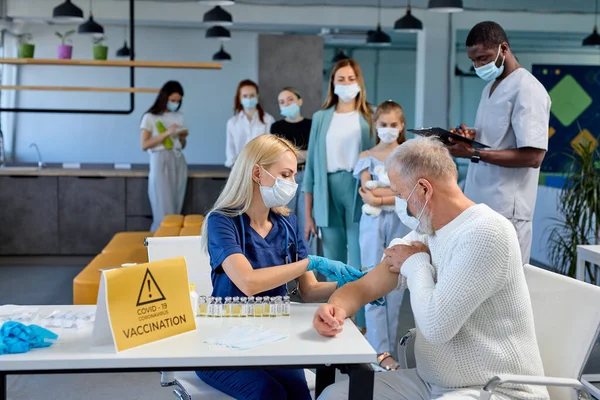 Läkare eller sjuksköterska ger ett injektionsvaccin mot covid-19 till äldre män — Stockfoto