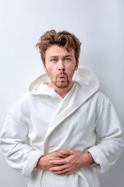 Young bearded man wearing bathrobe with hand on stomach because indigestion — Stock Photo, Image