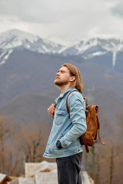 Bello maschio caucasico in giacca di denim sta guardando lato in contemplazione delle montagne — Foto Stock