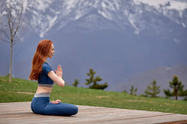 Молодая женщина сидит на улице в позе йоги и медитирует, держит руки вместе — стоковое фото