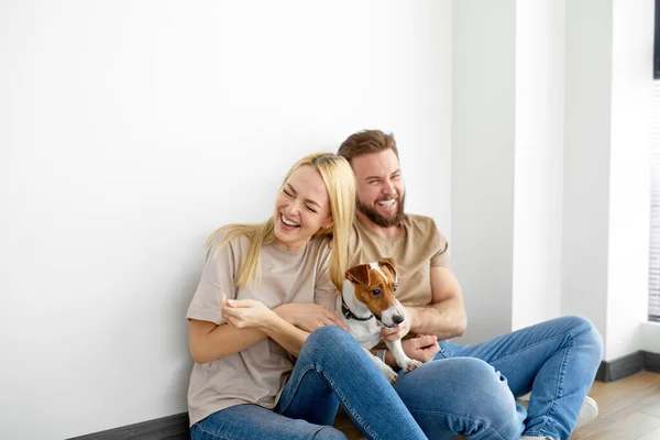 Alegre pareja caucásica familia sentarse en el suelo jugando con el perro mascota, divertirse, disfrutar de los fines de semana — Foto de Stock