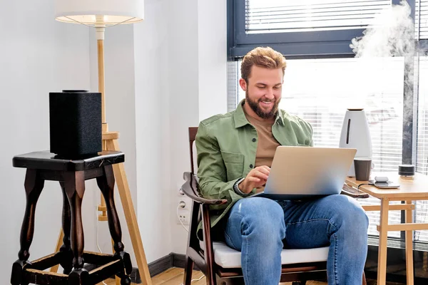 Mann arbeitet am Laptop im Raum mit tragbarem Lautsprecher, Luftreiniger, im Smart House allein — Stockfoto