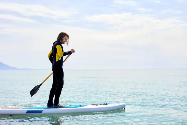 Vista lateral del hombre en traje de neopreno negro con paleta en la subtabla flota en el agua en el océano —  Fotos de Stock