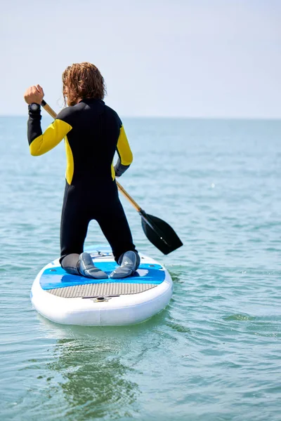 Vista trasera en forma joven que entra en el mar o el océano para surfear, sosteniendo paletas en las manos —  Fotos de Stock