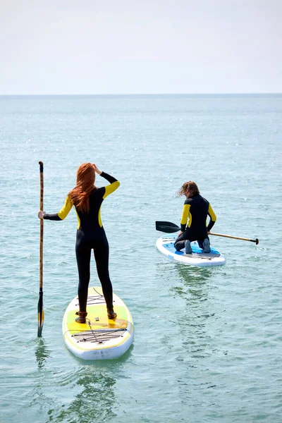 Mujer joven y hombre remando en SUP bordo en el mar en el día soleado —  Fotos de Stock
