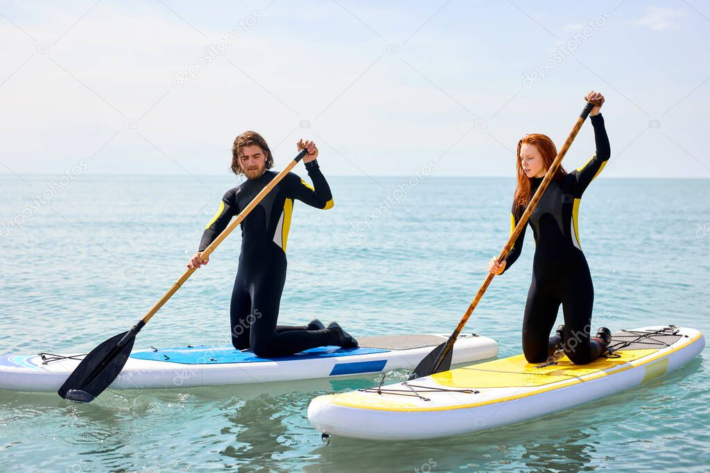 Happy beautiful young couple with paddle board at sea. Summer, vacation, surfing