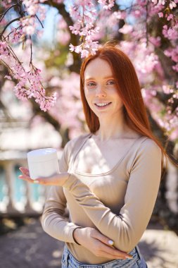 Gülümseyen kadın bahar bahçesinde poz veriyor yaz güneşinin ve doğanın tadını çıkarıyor, kozmetik kullanıyor.