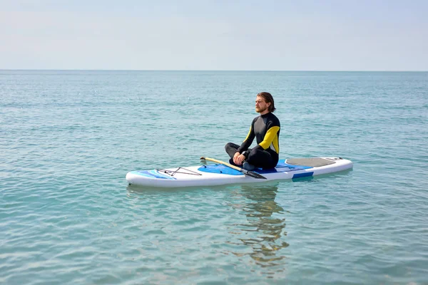 Porträt eines entspannten bärtigen Mannes, der nach dem Surfen auf dem Paddleboard sitzt und meditiert — Stockfoto