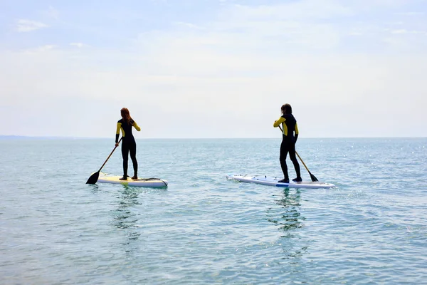Visão traseira no paddleboarding jovem casal em forma no mar, no paddleboard na água azul — Fotografia de Stock