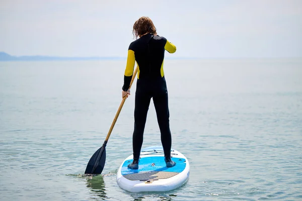 Vue arrière sur ajustement jeune homme entrant dans la mer ou l'océan pour surfer, tenant des pagaies dans les mains — Photo