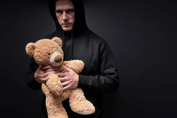 Man with frightening look holding teddy in hands, toy is simulating child abuse