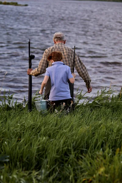 El nieto y el abuelo van a pescar juntos en la orilla del río. vacaciones de verano, generación —  Fotos de Stock