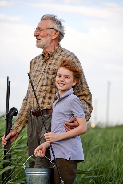 Lächelnde Rotschopf-Junge genießen Angeln mit Großvater, auf dem Land, Seitenansicht — Stockfoto