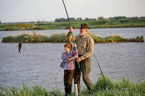 Amistoso buen abuelo y nieto tirando de la caña mientras pesca en fin de semana — Foto de Stock