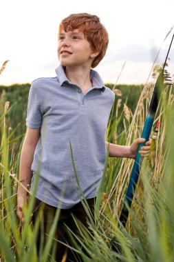Kibar kızıl saçlı çocuk elinde olta tutarak balık tutuyor.