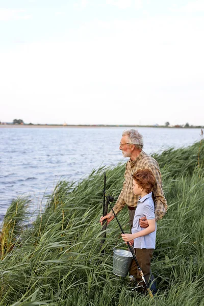 Little caucasian child boy with experienced old grey-bearded granddad going near lake — Stock Photo, Image