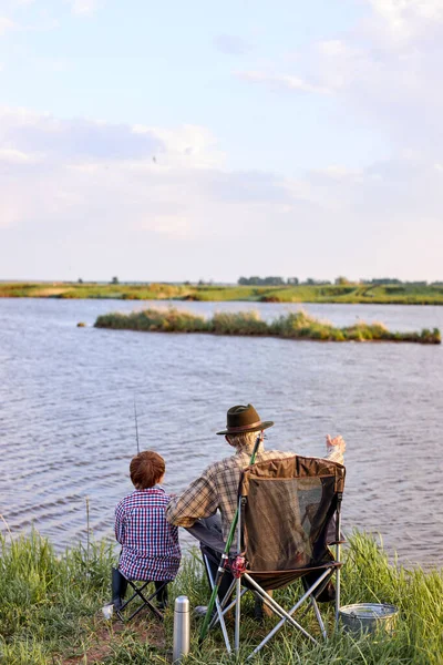 Homme âgé avec adolescent se détendre au bord du lac, aller pêcher. vue arrière — Photo