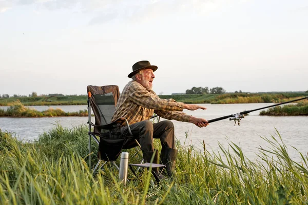 Homem idoso pescando no lago, pescando como hobby, retrato de vista lateral, no campo — Fotografia de Stock