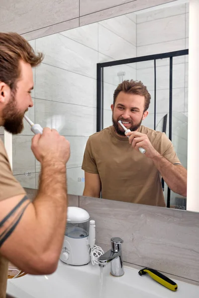 Young caucasian man brushing teeth with electric toothbrush during morning hygiene