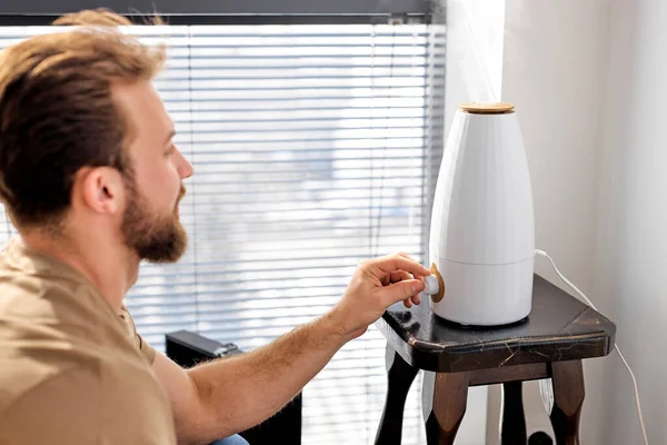 Smart Luftbefeuchter emittiert Wasserdampf auf dem Tisch, bärtige Mann verwenden schalten Sie ein modernes Gerät — Stockfoto