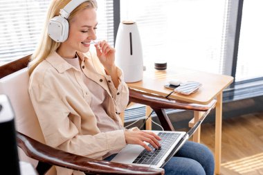 Evde çalışıyor, akıllı çalışıyor. Güzel kadın dizüstü bilgisayar ve modern cihazlar kullanıyor.