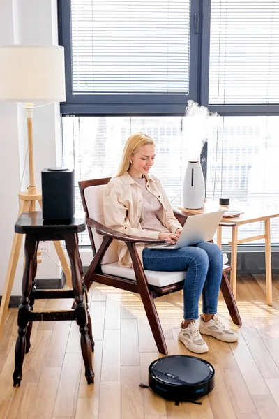 Blonde kaukasische Frauen arbeiten am Laptop und verwenden intelligente Staubsauger, Luftbefeuchter — Stockfoto