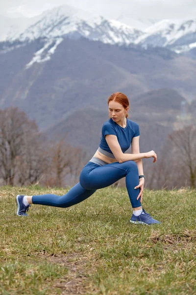 スポーツの制服の良い女性は足の筋肉を伸ばすために肺運動を行います — ストック写真