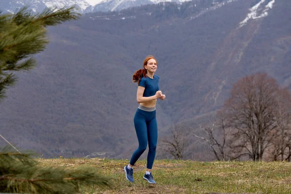 Jogging. Red-haired Female Runner during Outdoor Workout in nature, side view