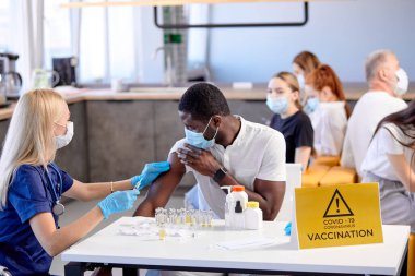 Hastane ofisindeki melez insanların toplu aşısı. Hemşire koruyucu giysi iş başında.