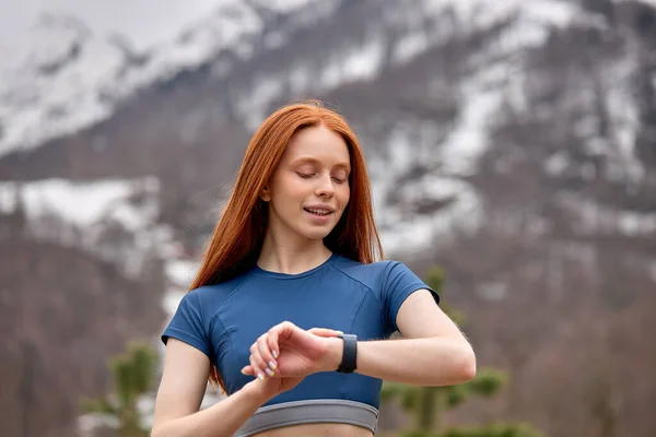 Sportieve jonge roodharige vrouw op zoek naar horloges, het controleren van de tijd na het lopen tijdens de training — Stockfoto
