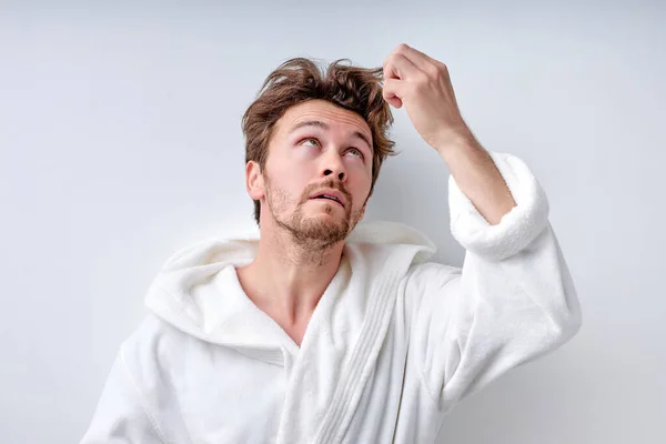 Jovem desgrenhado em roupão de banho isolado no fundo branco, toca o cabelo longo regrown — Fotografia de Stock