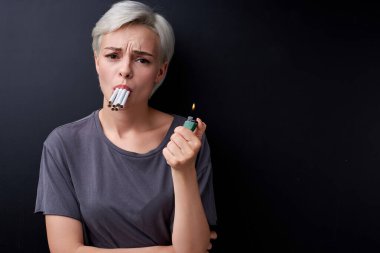 Depresyonda bir kadın ağzında bir sürü sigara tutuyor ve iğrenerek kameraya bakıyor..