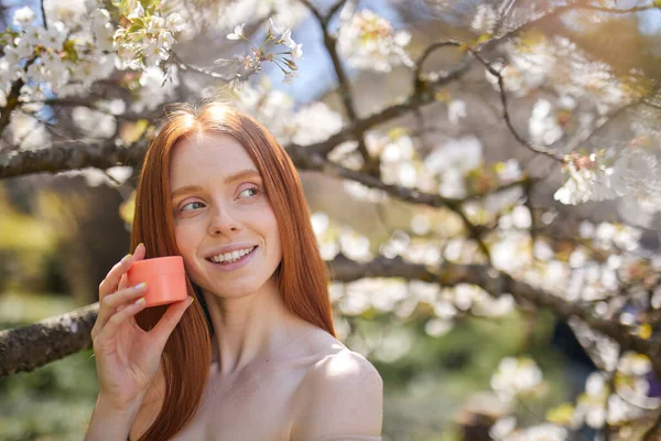 Gros plan portrait de femme caucasienne détendue tenant pot de crème dans les mains dans la nature — Photo