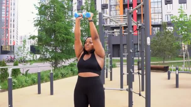 Afro overgewicht fitness vrouw doet workout met halters outdoor, in sportieve outfit — Stockvideo