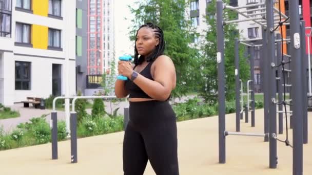 Africana grasa fitness hembra haciendo ejercicio con mancuernas al aire libre, usando equipo deportivo — Vídeo de stock