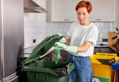 Güzel kızıl saçlı kadın plastik şişeleri çöp tenekesine ayırıyor, gezegeni kurtarıyor, çevre dostu insan...